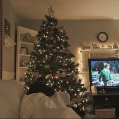 a living room with a christmas tree in the corner and a tv on top of it