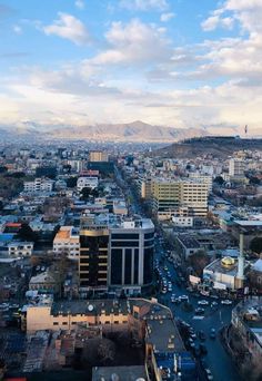 an aerial view of a large city with mountains in the backgrouund and cars on the road