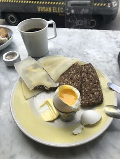 a plate with bread, eggs and butter on it next to a cup of coffee