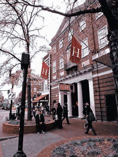 people walking on the sidewalk in front of a building with red flags hanging from it