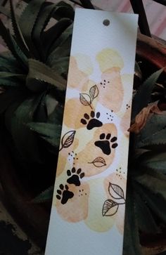 a bookmark with dog paw prints on it sitting next to a potted plant