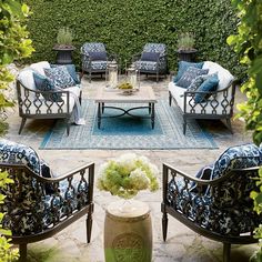 an outdoor seating area with blue and white cushions, chairs, and a table surrounded by greenery