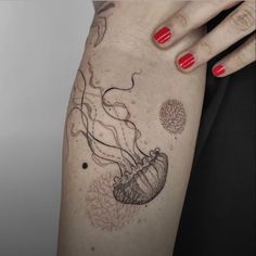 a woman's arm with a jellyfish tattoo on her left thigh and red nail polish