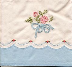 a blue and white table cloth with pink roses on the border, embroidered onto it