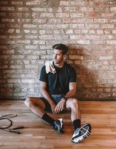 a man sitting on the floor in front of a brick wall wearing black and white shoes