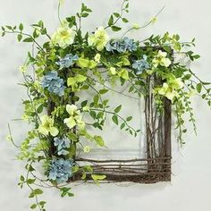 a wreath made out of branches with flowers and greenery on the front, against a white wall