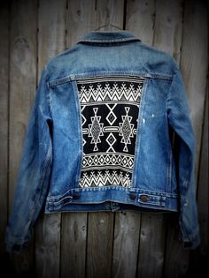 a denim jacket with an embroidered design on it hanging up against a wooden wall in front of a door