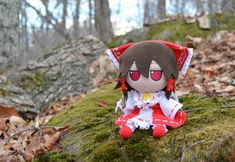 a stuffed animal doll sitting on top of a moss covered rock in the woods with red eyes