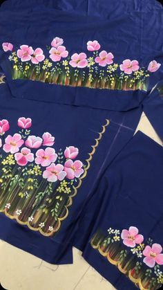 three blue shirts with pink flowers painted on the front and back, sitting on a table