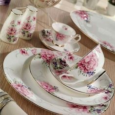 a table topped with lots of white and pink plates covered in floral design on top of a wooden table