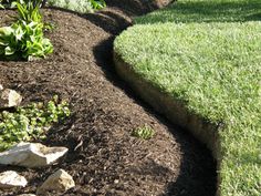 a garden with grass, rocks and flowers in the ground next to a path that has been dug into it