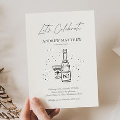 a hand holding up a wedding card with a wine bottle on it