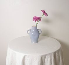 a blue vase sitting on top of a white tablecloth with pink flowers in it