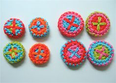 six crocheted buttons are arranged on a white surface, each with different designs