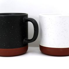 two black and white coffee mugs sitting next to each other on a white surface