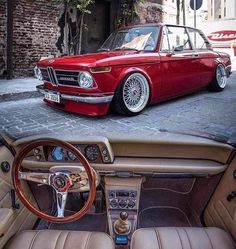 an old red car parked in front of a brick building with its door open and the interior