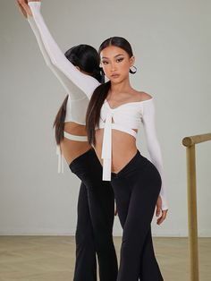 two women in white top and black pants posing for the camera with their arms around each other