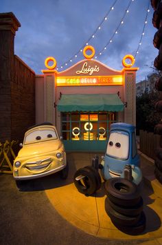 two cars parked in front of a building with lights strung over the entrance to it