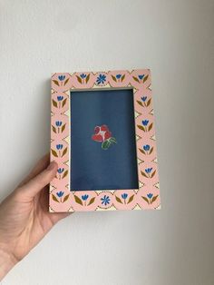 a hand holding a small pink frame with flowers on it