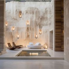 a room with some lights on the wall and a pool in the middle that is surrounded by stone walls