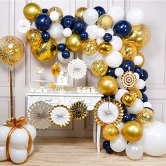 a table topped with balloons and other items next to a wall covered in gold, white and blue decorations