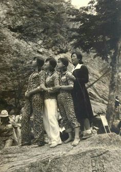 an old black and white photo of four women standing on top of a rock with trees in the background