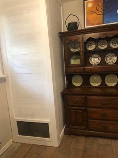 an old wooden china cabinet with plates on it's top and bottom shelf next to a door