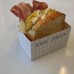 an egg, bacon and cheese sandwich in a paper box on a white countertop