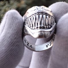 a person wearing a silver ring with an open mouth and words engraved on the side