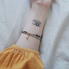 a woman's arm with a camera tattoo on it, and a black beaded bracelet