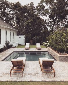 two lawn chairs sitting next to a swimming pool in the middle of a backyard area