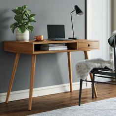 a desk with a laptop on it in front of a chair and wall mounted painting