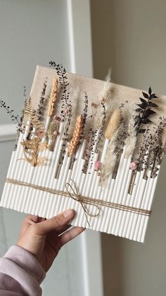 a person holding up a card with dried plants on it