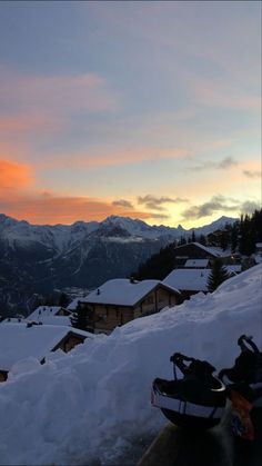 snowmobiles parked on the side of a snowy hill at sunset with mountains in the background