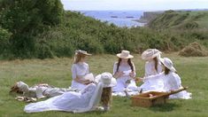 three women in white dresses and hats sitting on the grass with their backs to each other