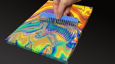 a person is holding a comb in front of a colorful design on a piece of paper