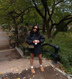 a woman is standing on the steps in front of some trees and holding a cup