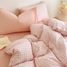 an unmade bed with pink gingham sheets and pillows