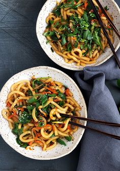 two bowls filled with noodles and vegetables on top of a table next to chopsticks