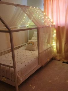 a bed with a white canopy and some lights on the wall behind it in front of a window