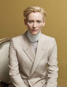 a woman sitting on top of a white chair wearing a suit and turtle neck sweater