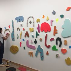 a woman standing next to a white wall covered in colorful cut out letters and shapes