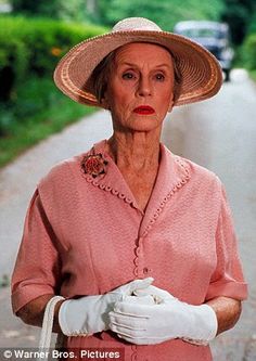 an older woman wearing white gloves and a pink shirt is standing on the side of a road