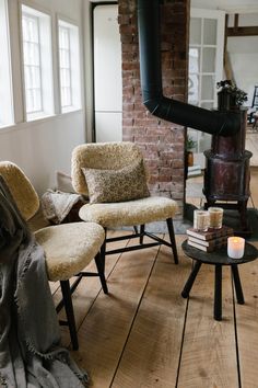 two chairs and a table in front of a brick wall with a wood burning stove