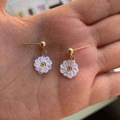 a hand holding two small white flower earrings