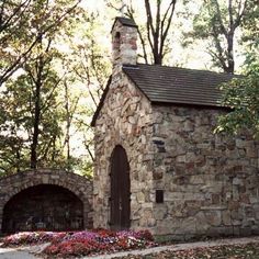 an old stone church surrounded by trees and flowers