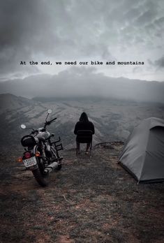 a motorcycle parked next to a tent on top of a hill with a person sitting in the background