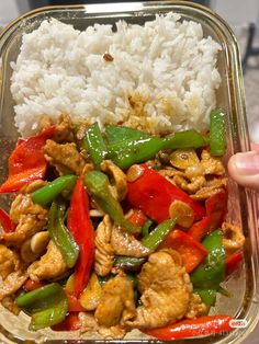 a person holding up a container filled with rice and veggies