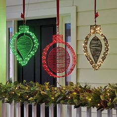 three christmas ornaments hanging from the side of a house decorated with lights and greenery