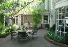 an outdoor patio with table and chairs surrounded by greenery on the side of a house